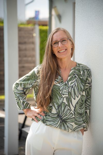 Heilpraktikerin Maike Hoyer im Garten vor ihrer Praxis für Naturheilkunde Maike Hoyer lehnt an der Außenwand zu ihrer Praxis für Naturheilkunde